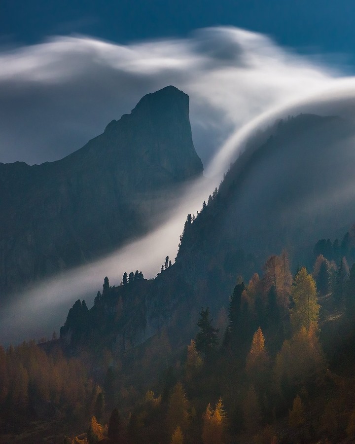 A mountain summit rises above a cloud-filled valley in the Dolomites.