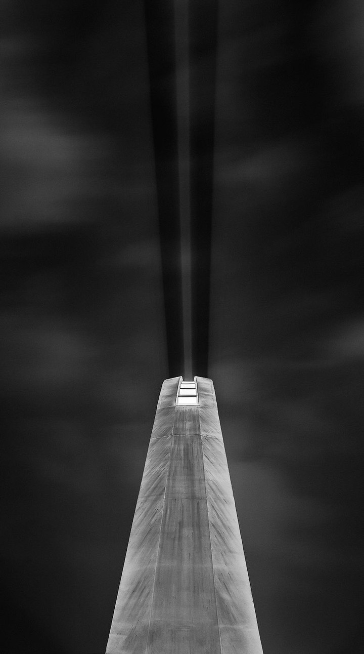 A lit bridge pylon and converging cables rise vertically into a dark sky.
