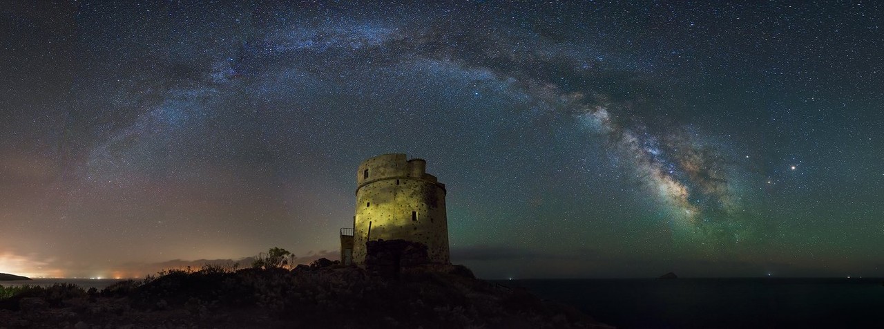 A coastal watchtower stands in silhouette beneath the Milky Way.